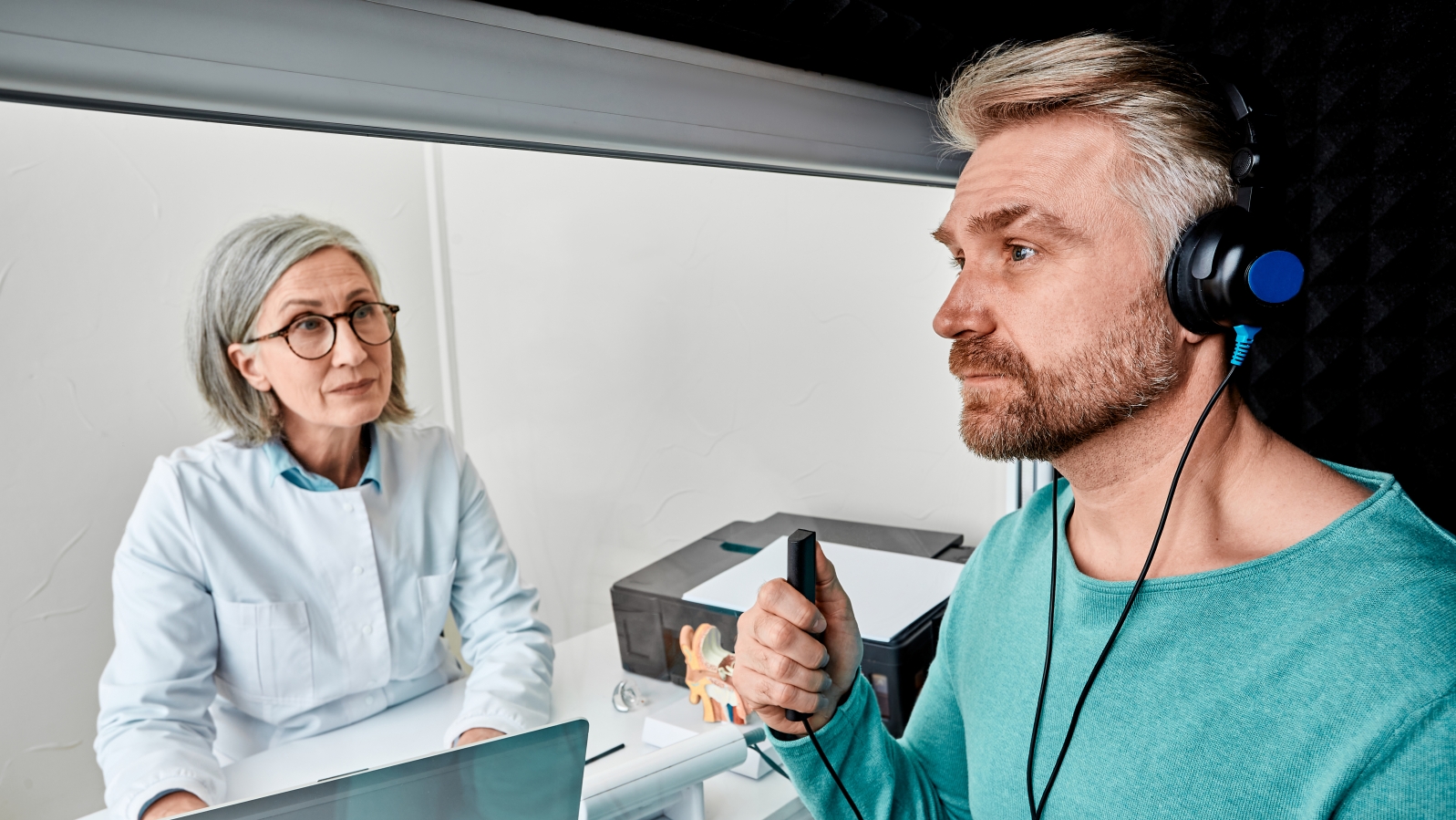 Male patient wearing audiology headphones pressing button of response while audiometric testing in soundproof audiology booth. Hearing testing